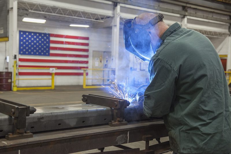 Man welding in a fab shop in front of an American flag