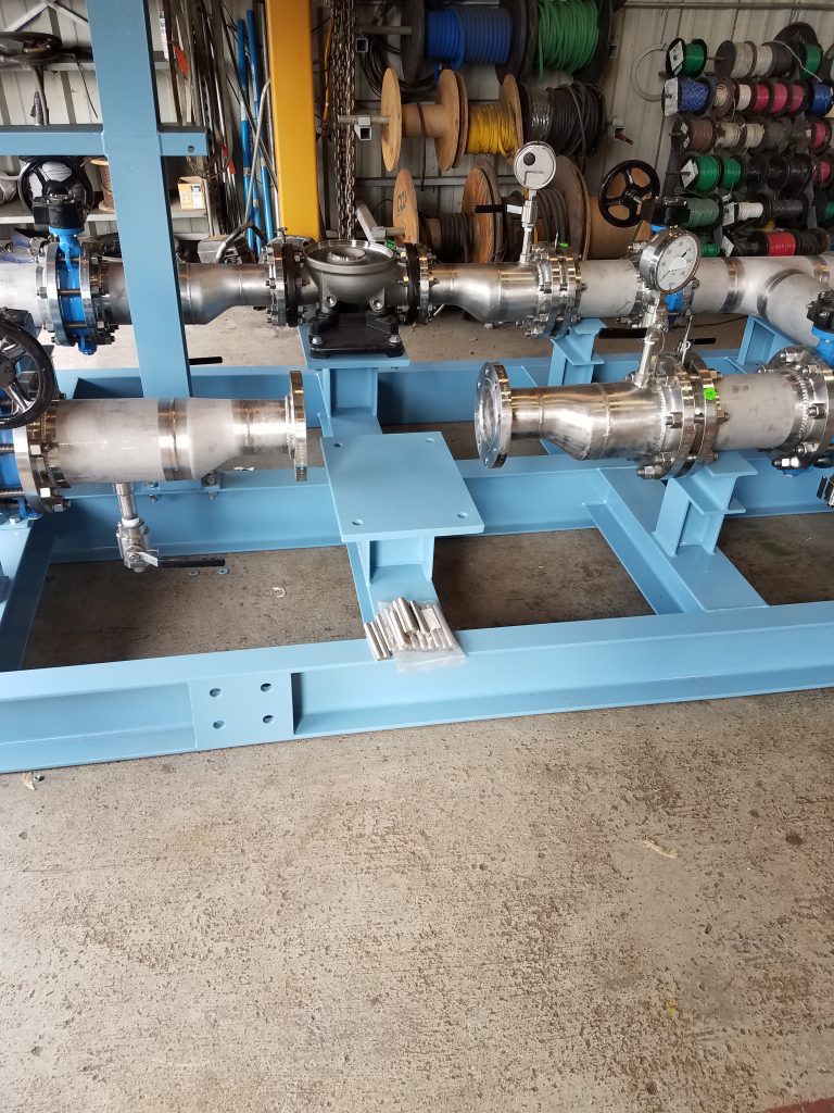 Close-up view of GSM Industrial's ozone injection piping skid showing stainless steel piping, valves, gauges, and carbon steel frame in a workshop setting