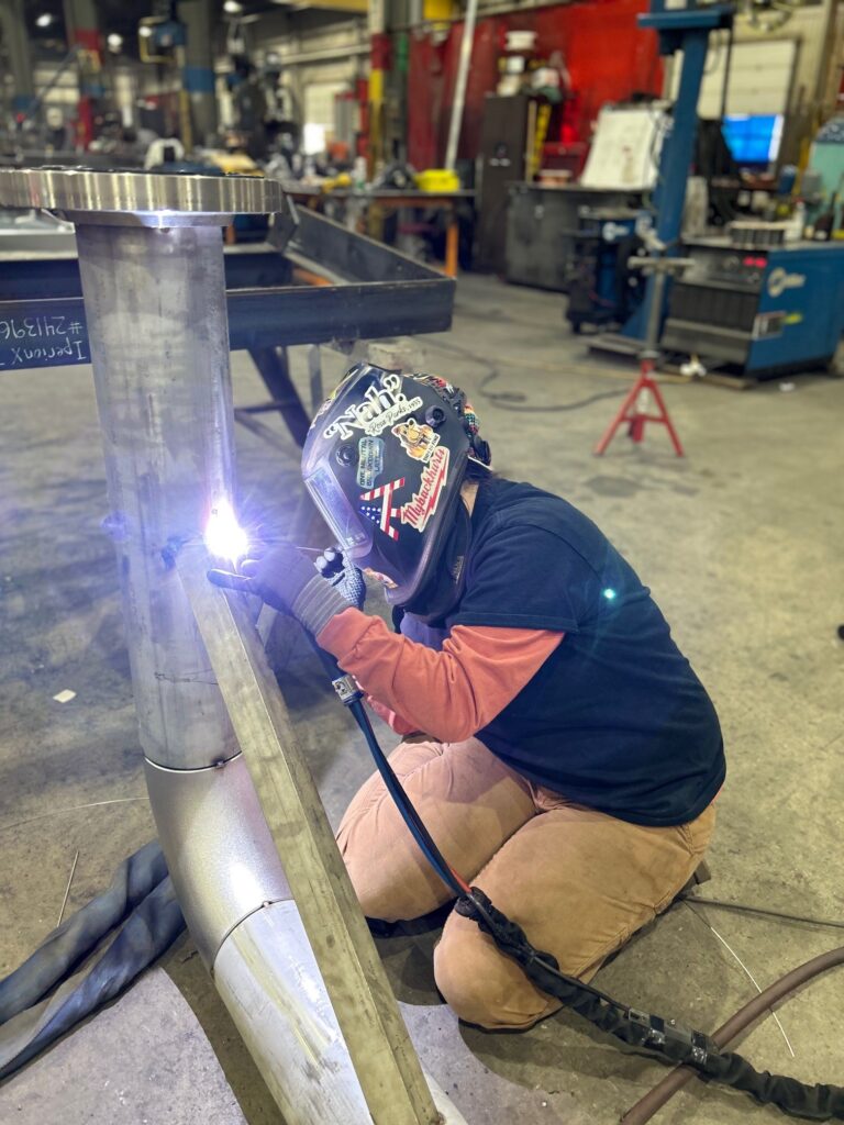 A welder performs precise TIG welding on stainless steel piping inside the GSM Industrial fabrication shop, using a torch and filler rod for clean, high-quality welds.