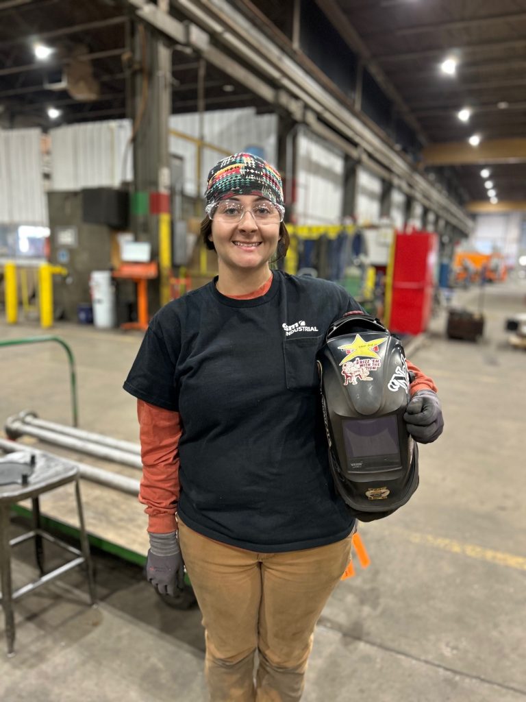 Portrait of Danielle, a welder at GSM Industrial, wearing her welding helmet and safety gear.