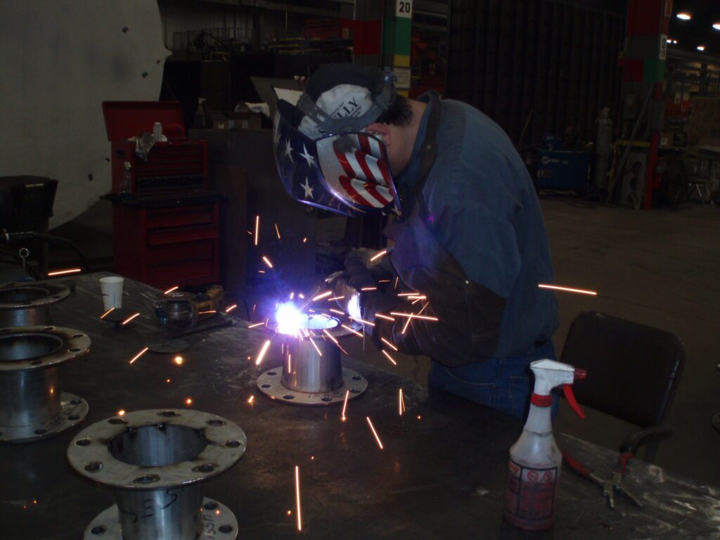 A welder performs MIG welding on metal duct spools in the GSM Industrial fabrication shop, creating clean, consistent welds for industrial assemblies.