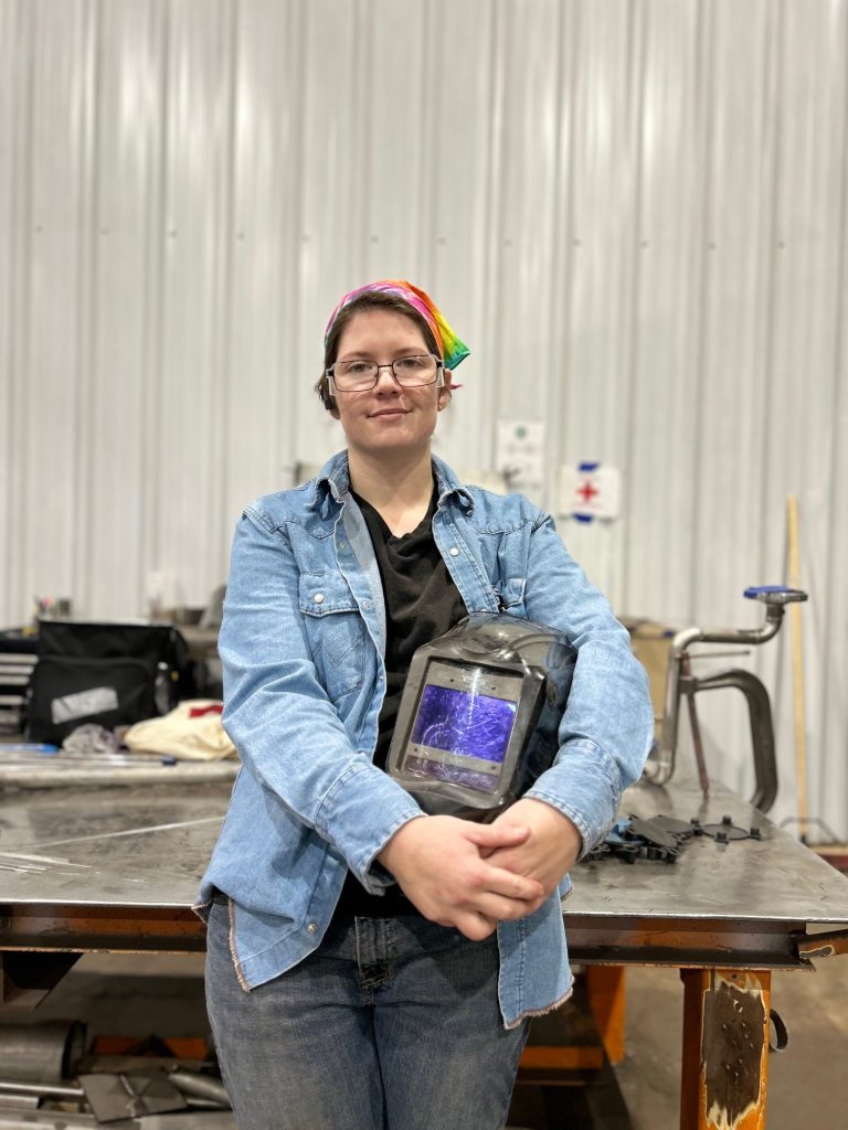Portrait of Megan, a welder at GSM Industrial, smiling confidently in her welding gear.