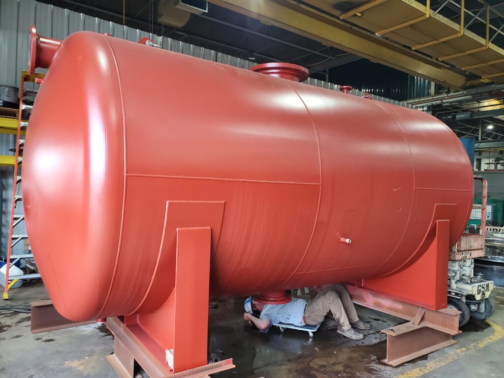 A GSM Industrial team member performs final assembly work on a large ASME-certified storage tank inside the fabrication shop.