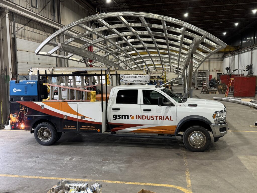 GSM Industrial service truck parked beside the massive stainless-steel canopy frame, illustrating the scale of the architectural project.
